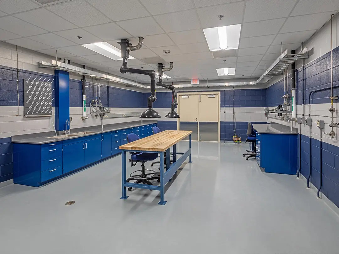 work room with central table and exhaust piping, peripheral cabinetry with sink and desk