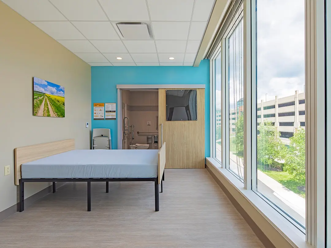 hospital room with bed, artwork, bathroom and view of trees outside