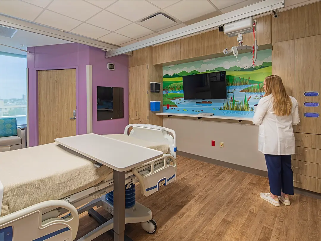 hospital room with bed, colorful mural, television and notice board