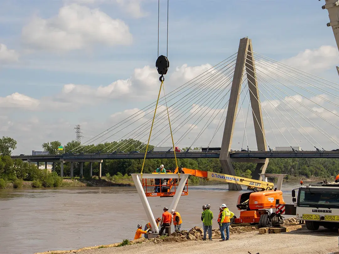 construction crane moving pedestrian bridge support structure into place on job site