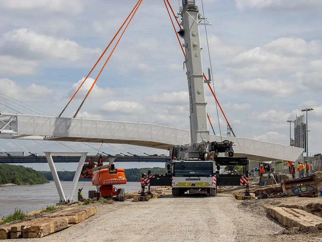 construction crane moving pedestrian bridge steel into place on job site