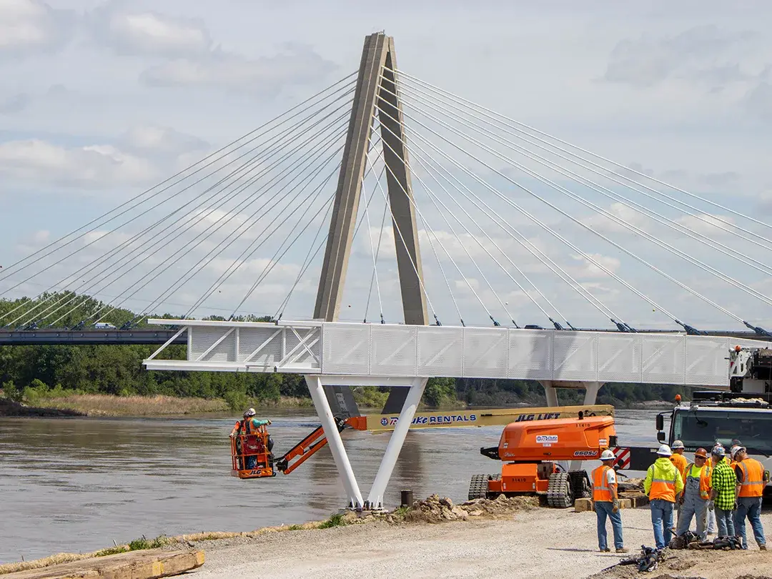 construction crane moving pedestrian bridge steel into place on job site