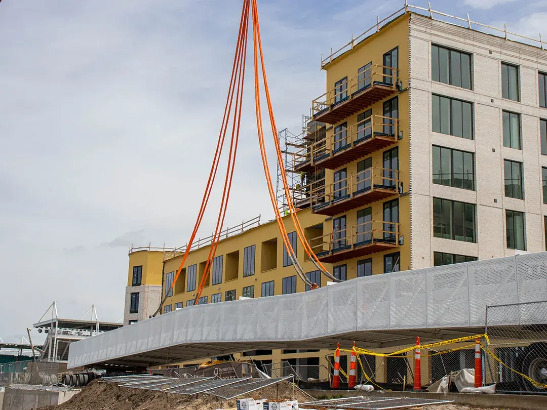 construction crane moving pedestrian bridge steel into place on job site
