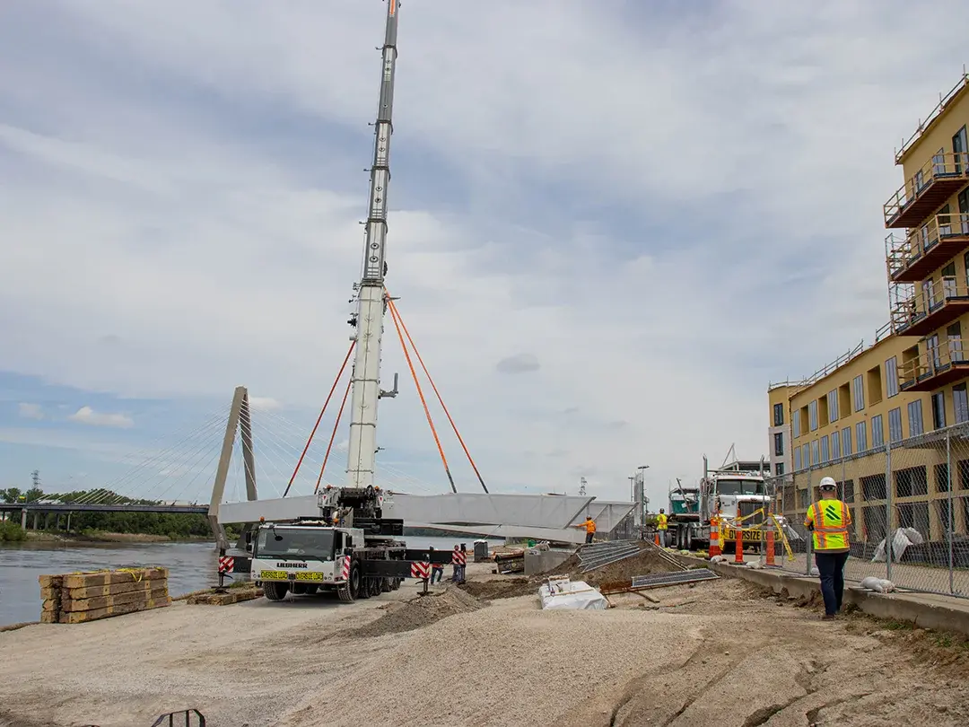 construction crane moving pedestrian bridge steel into place on job site