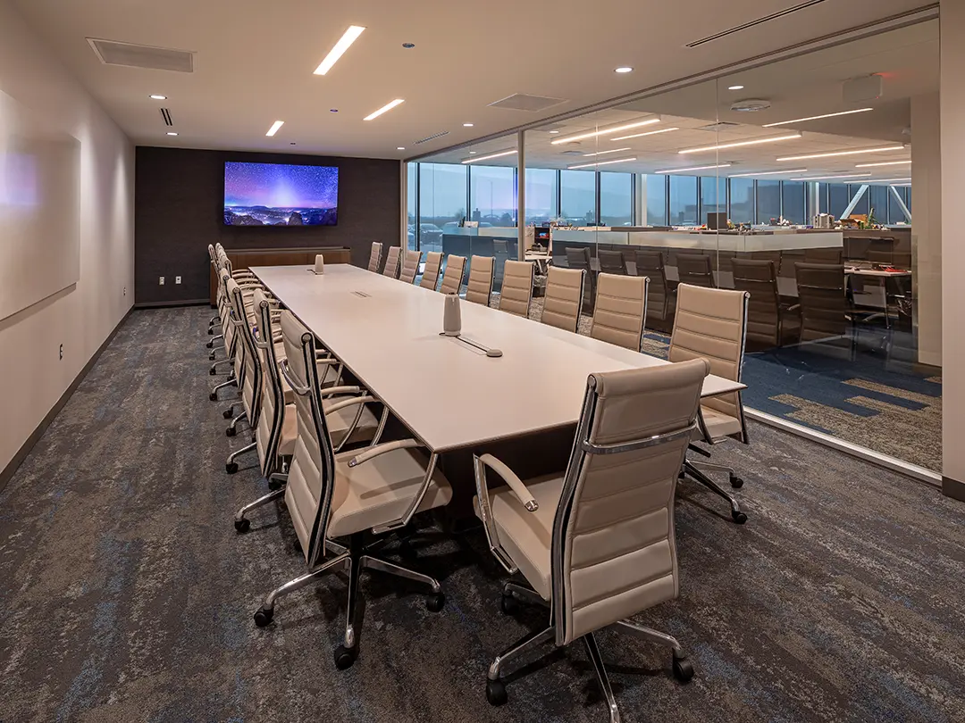 conference room with white chairs, large video screen and glass wall with view to work station area