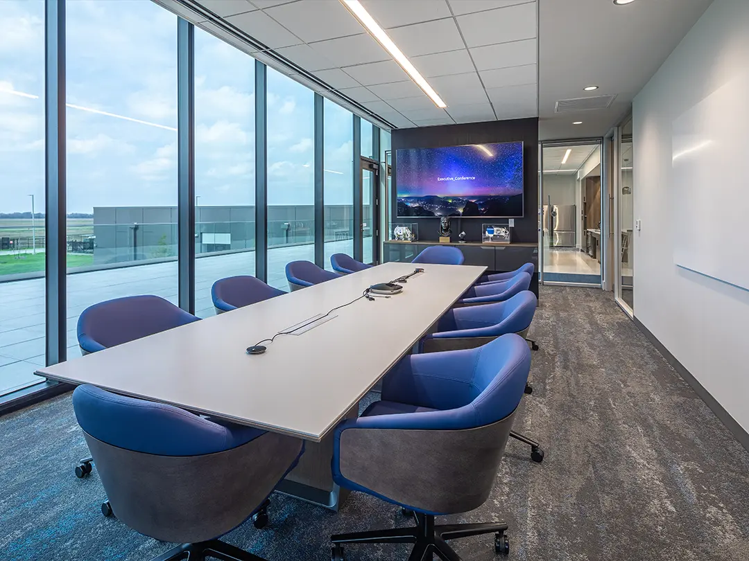 conference room with blue club chairs, large video screen and views outside and into adjacent kitchen