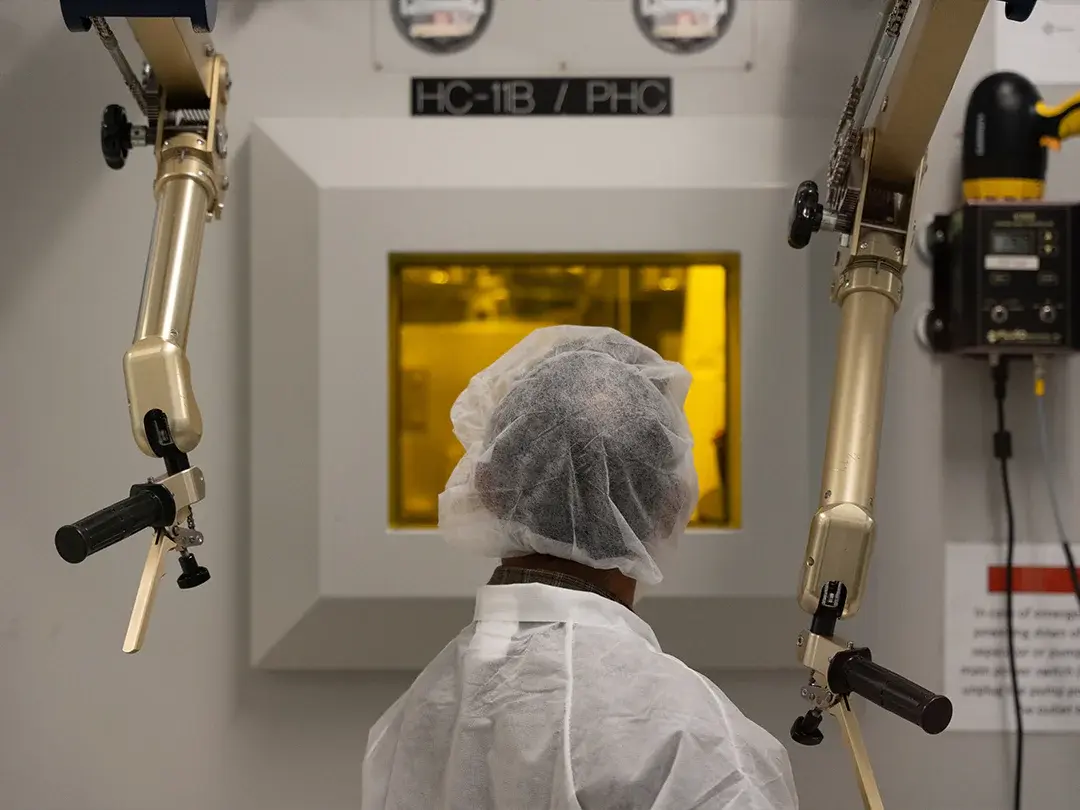 staff member looking through window, surrounded by system controls, wearing clothes and hair coverings
