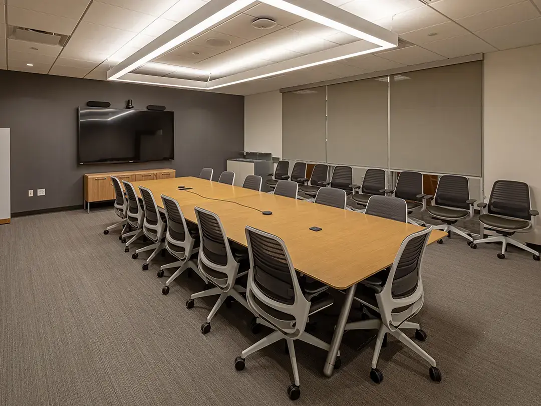 conference room with wooden table, large LCD screen, overhead lighting and extra seating