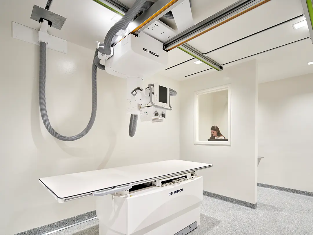 x-ray equipment and table with technician behind wall with window