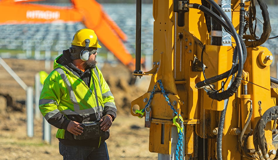 construction worker with protective gear with large equipment on solar site