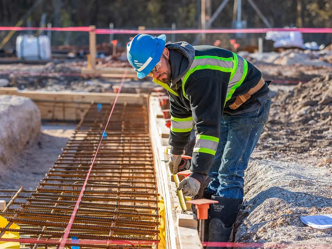 construction worker measures spacing of concrete rebar components