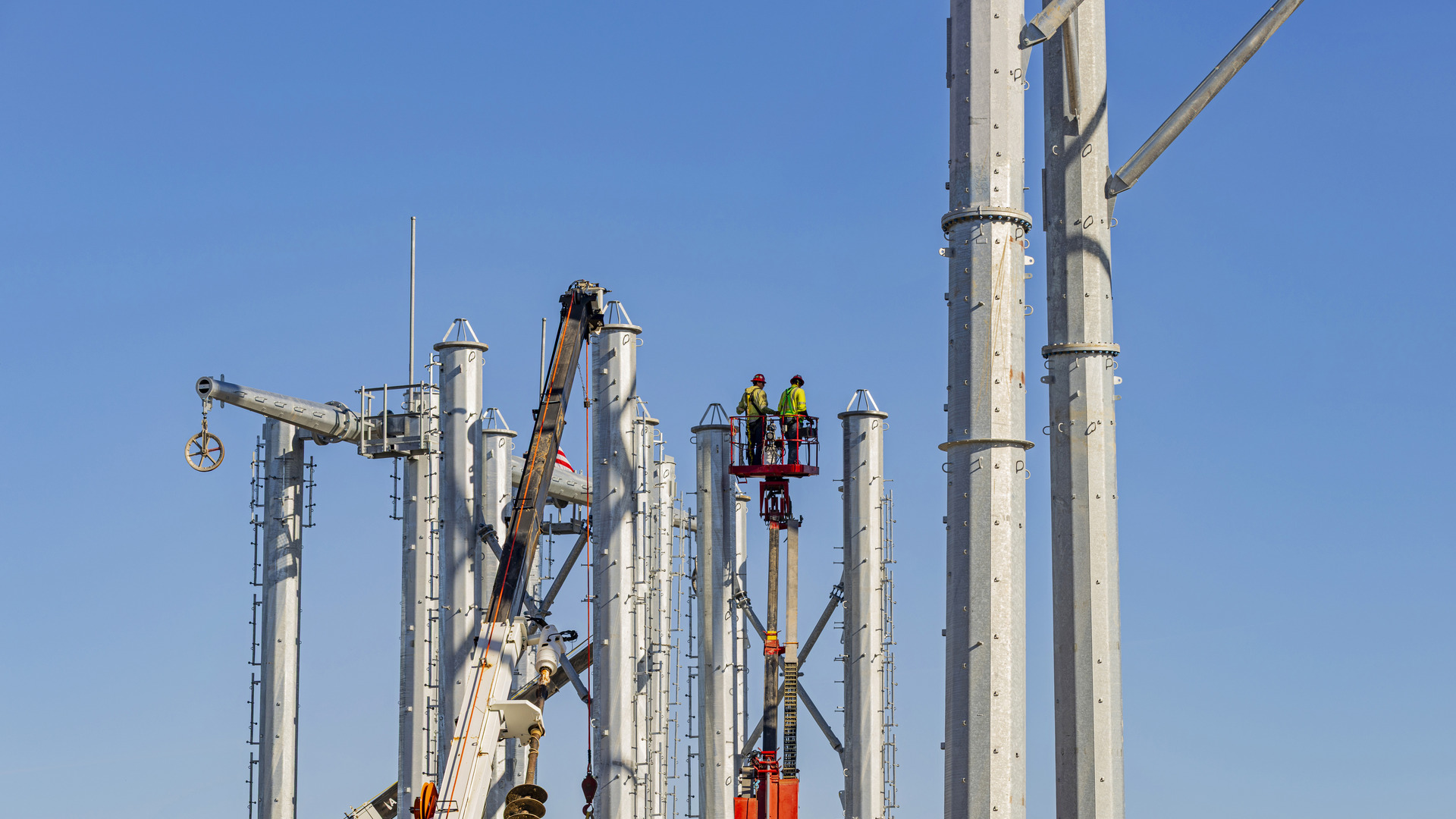 Workers in an aerial lift install equipment among tall steel telecommunications structures.