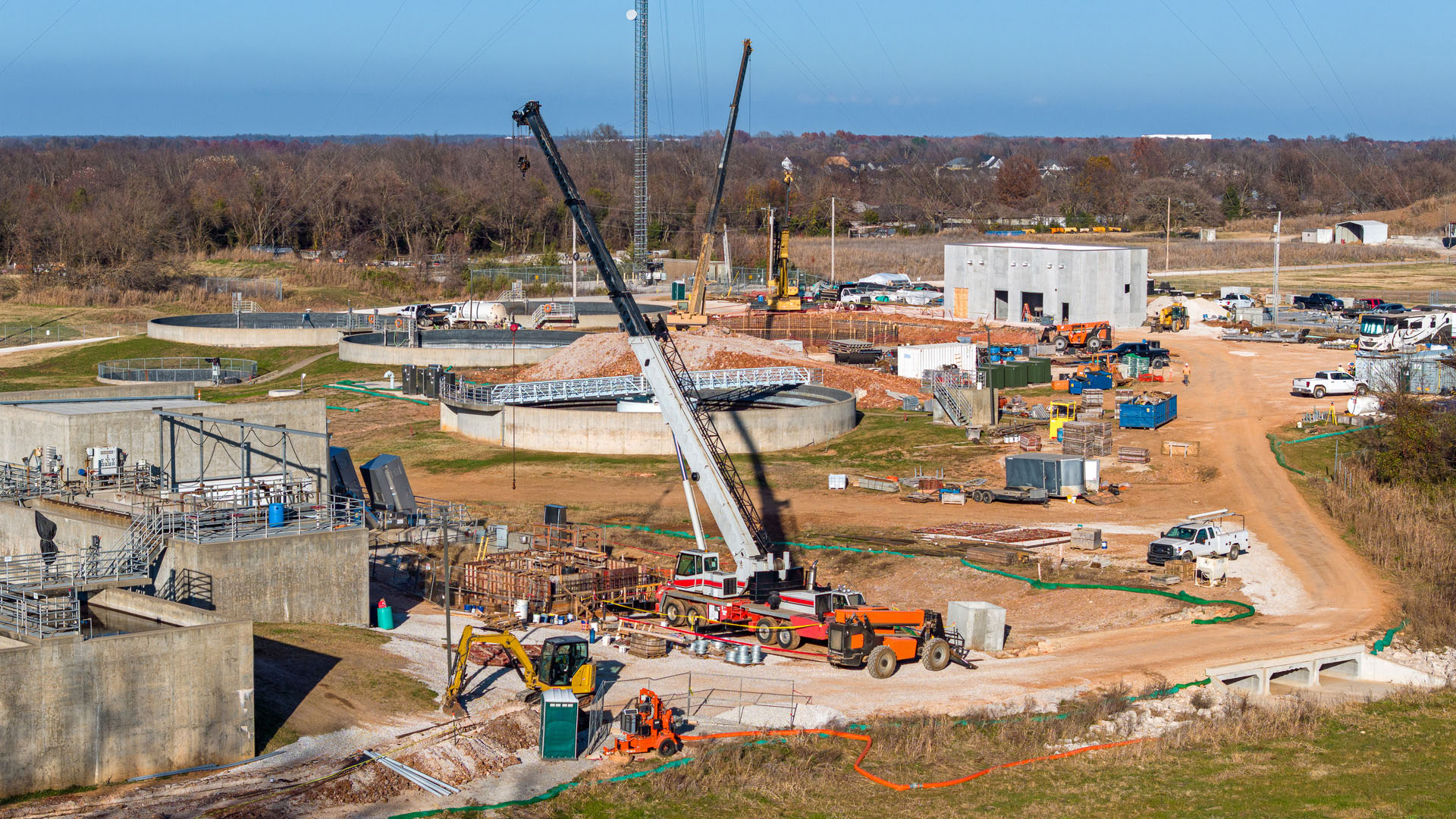 Water treatment facility under construction with cranes, circular tanks, heavy equipment and concrete structures spread across the site.