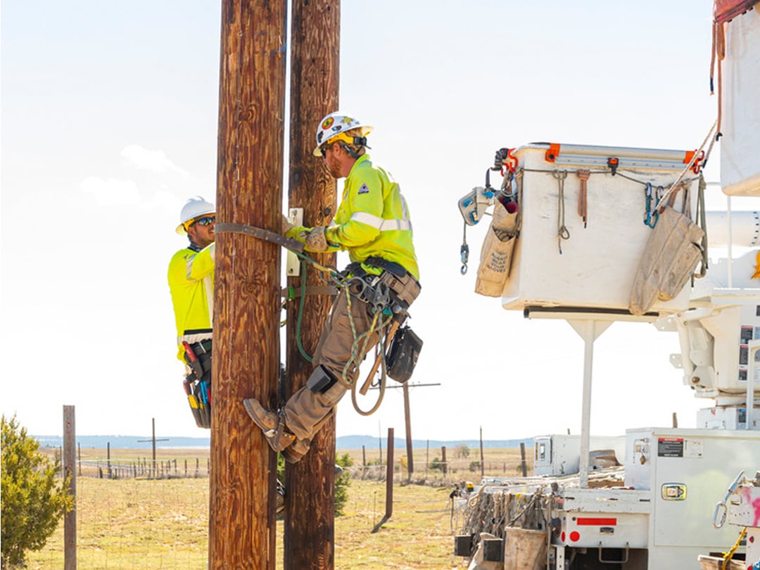 linemen working on wooden poles next to bucket truck